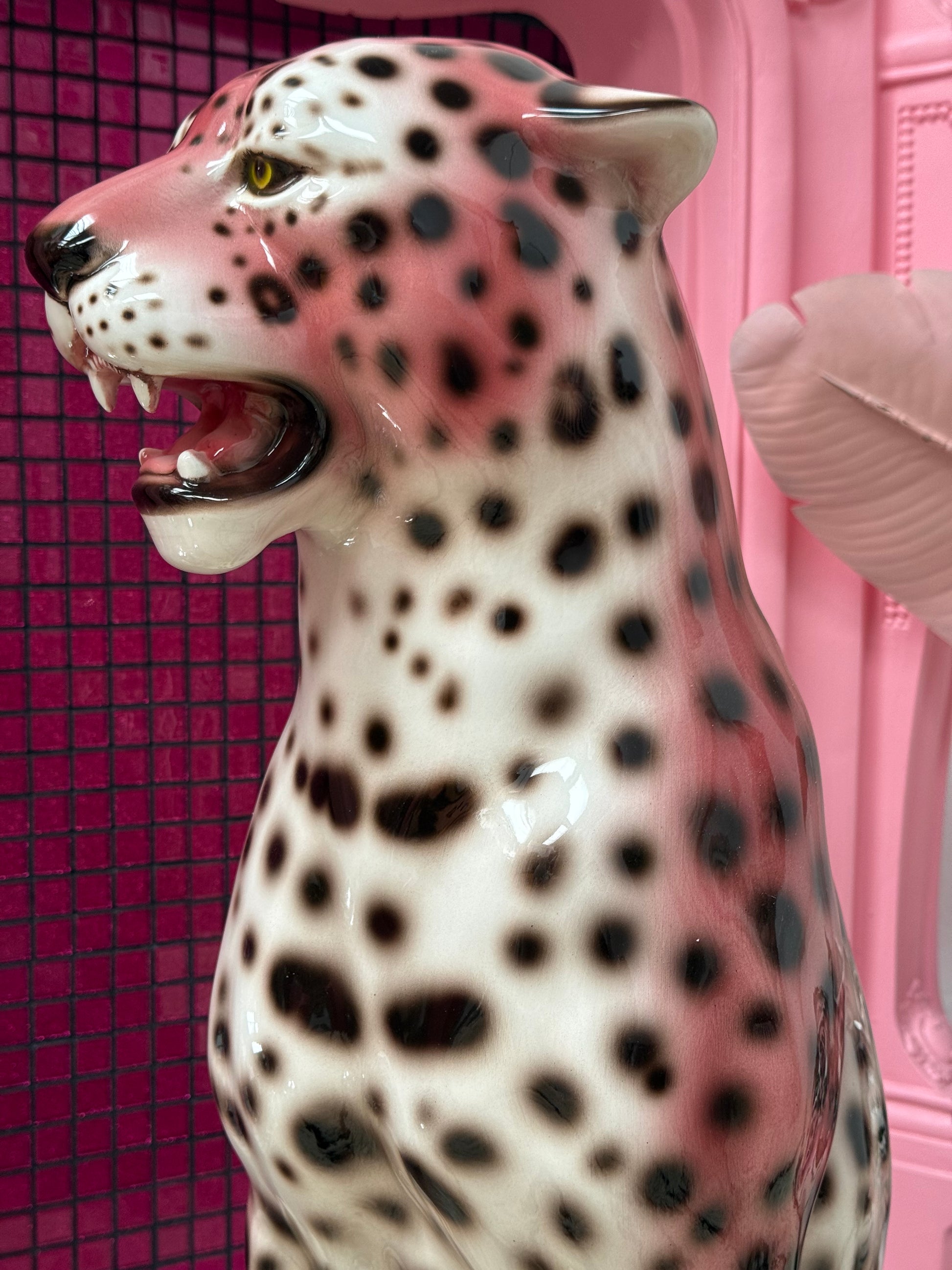 A glossy ceramic leopard figurine with a white body, black spots, and pink shading, shown close-up against a pink background.